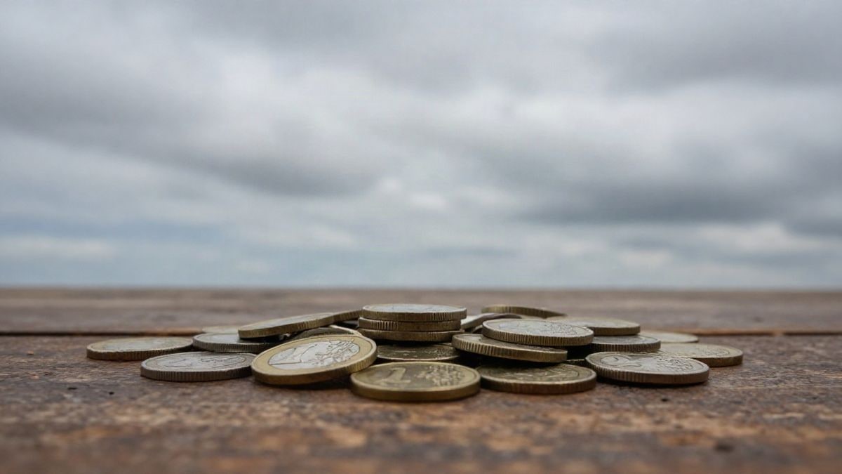 Imagen ilustrativa: monedas de euro apiladas sobre una mesa de madera con el cielo de fondo