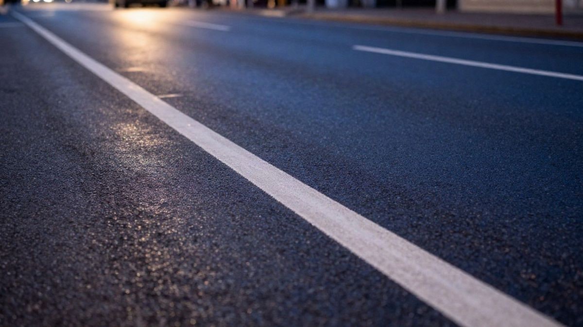 Imagen ilustrativa: asfalto mojado con marcas blancas de carril al atardecer