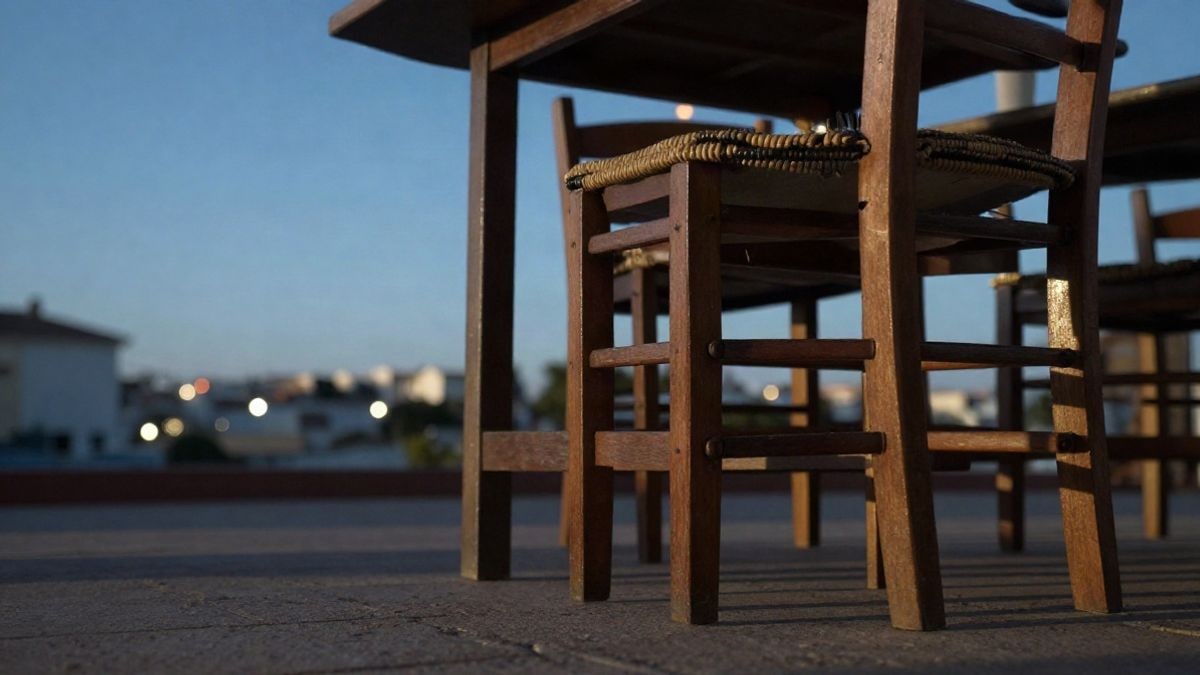 Imagen ilustrativa: patas de mesas de madera y una silla vacía en una terraza al atardecer