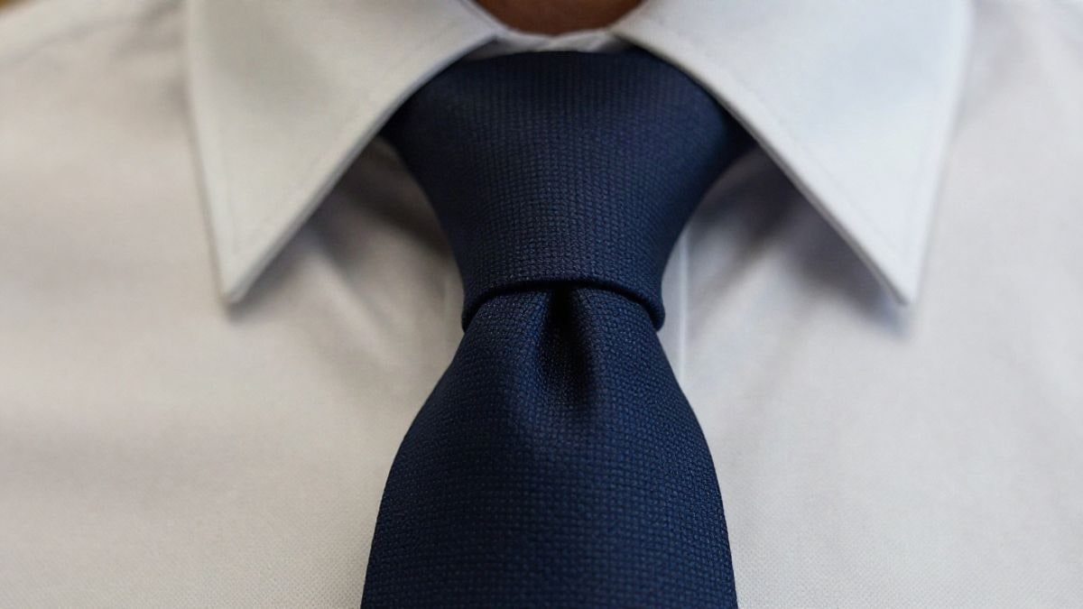Imagen ilustrativa: primer plano macro de un nudo de corbata azul sobre camisa blanca