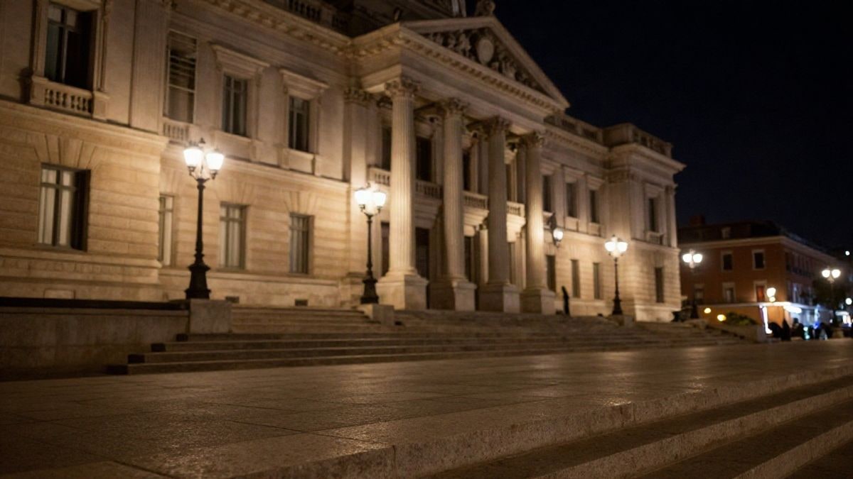 Imagen ilustrativa: fachada de un edificio institucional neoclásico iluminada por farolas y focos de noche