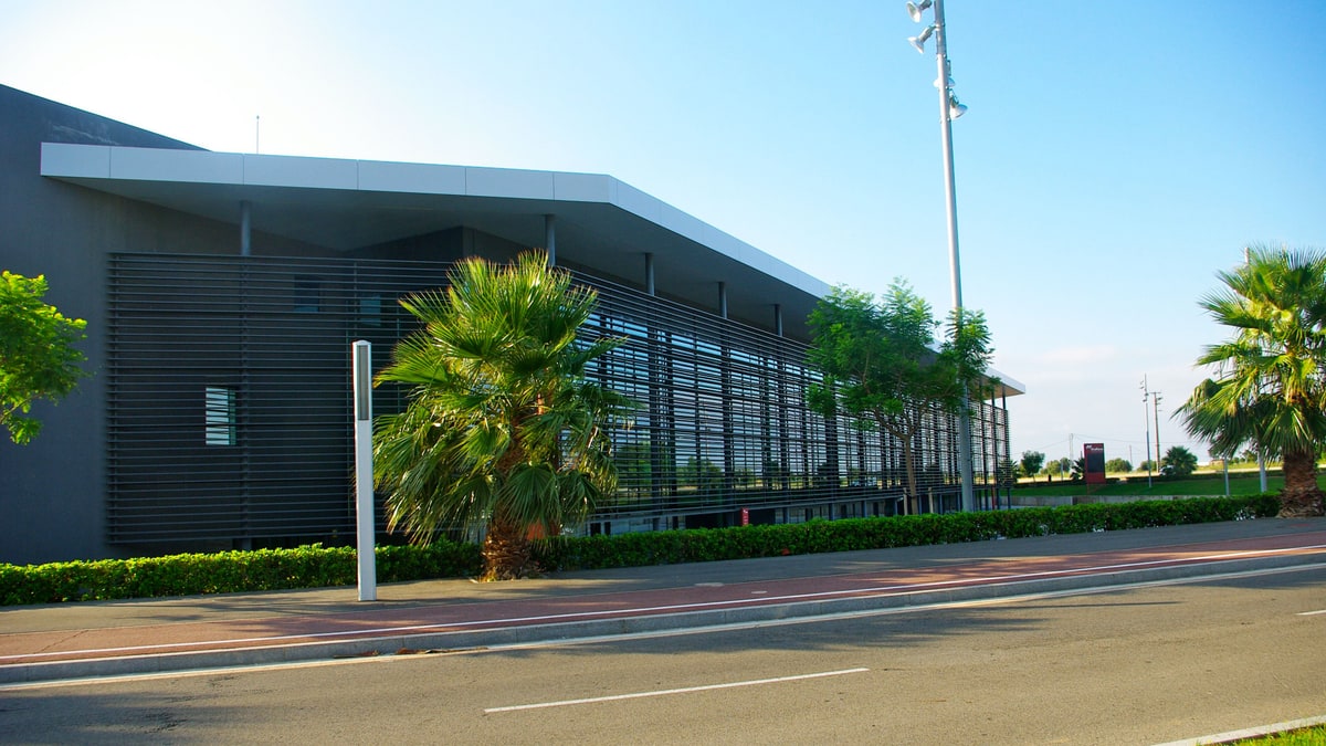 Exterior facade of the firaReus exhibition center, with metal slats, palm trees, and an avenue in front.
