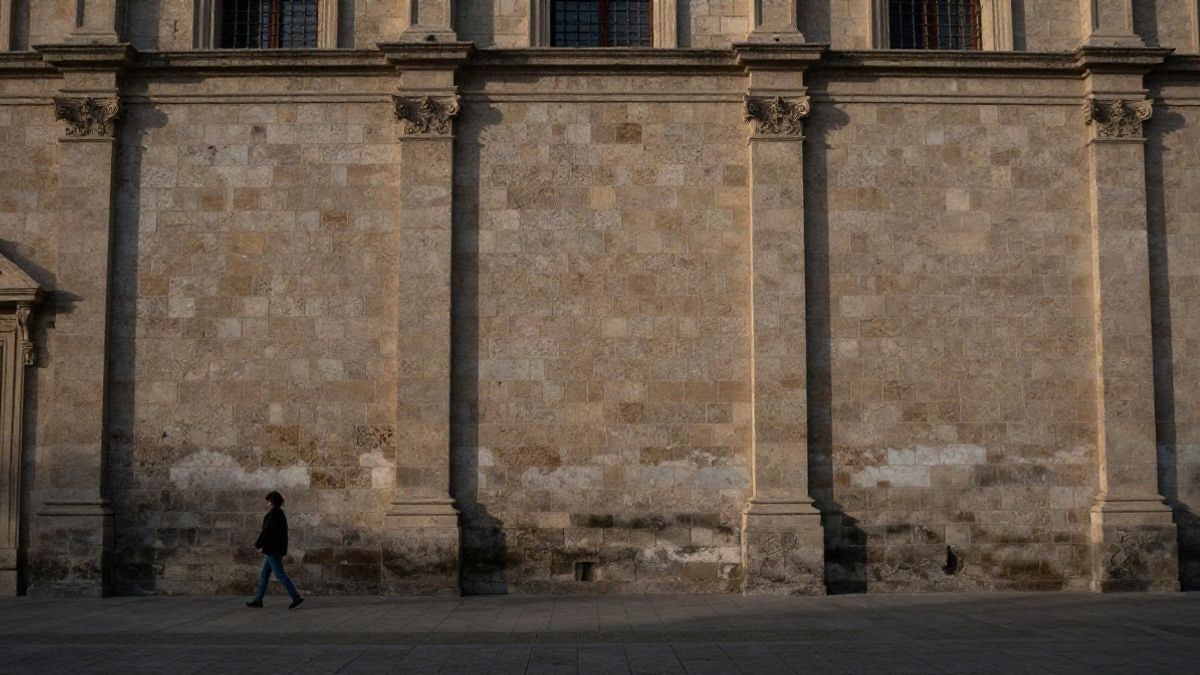 Illustrative image: facade of a historic stone building with a distant figure passing by at sunset