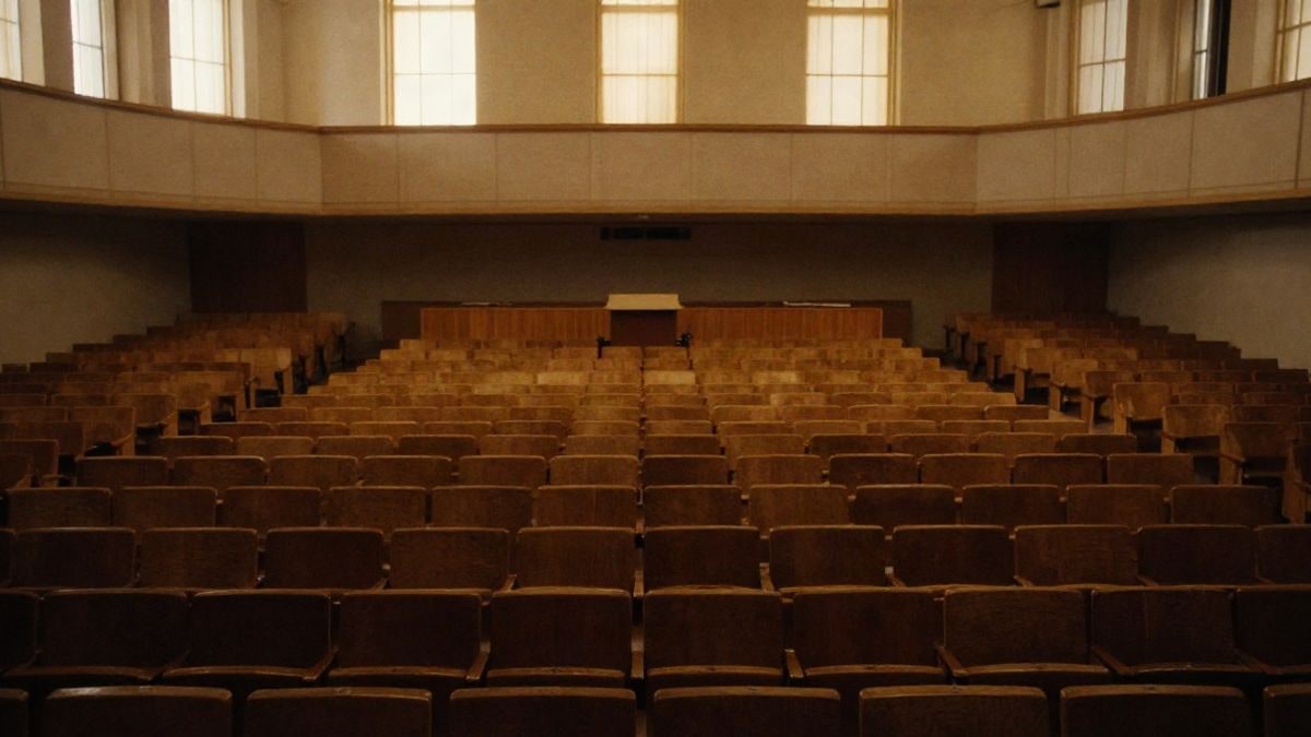 Imagen ilustrativa: un auditorio vacío con un atril en el escenario y luz natural entrando por los ventanales