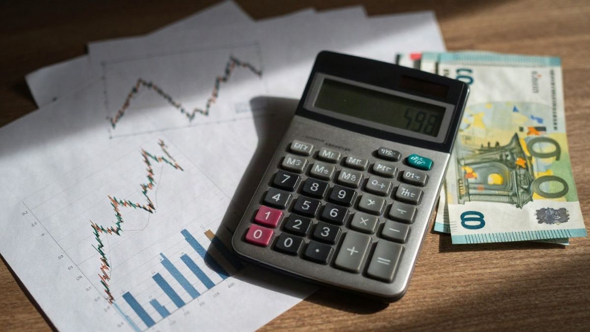 Illustrative image: overhead view of a calculator, financial graphs, and euro notes on a wooden table