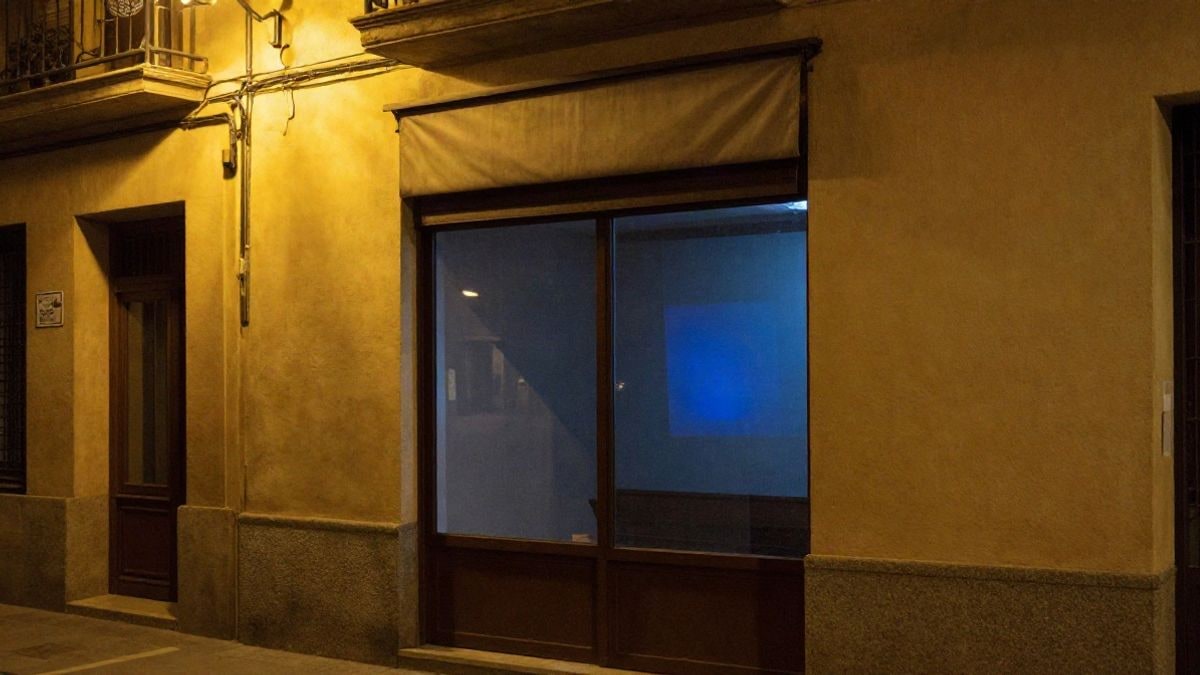 Imagen ilustrativa: calle comercial de noche iluminada por farolas, con un escaparate de luz azulada al fondo