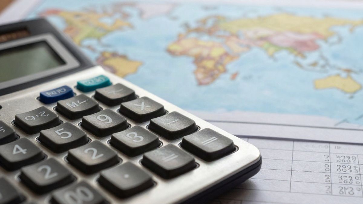 Illustrative image: close-up of a calculator and financial documents on a table, with a blurred world map in the background