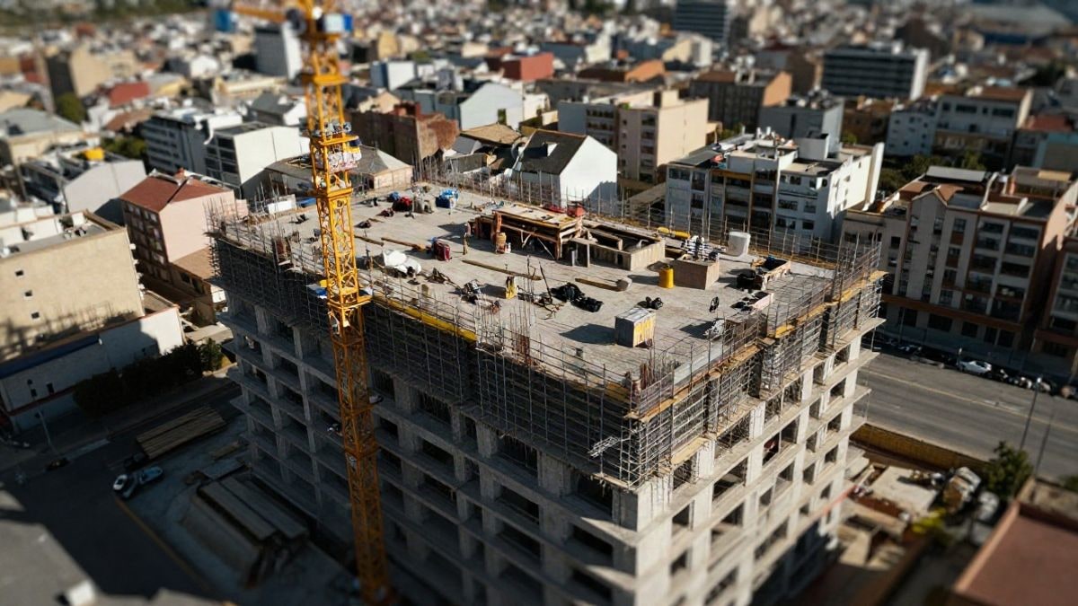 Illustrative image: aerial view of a residential building under construction with cranes and scaffolding in an urban setting