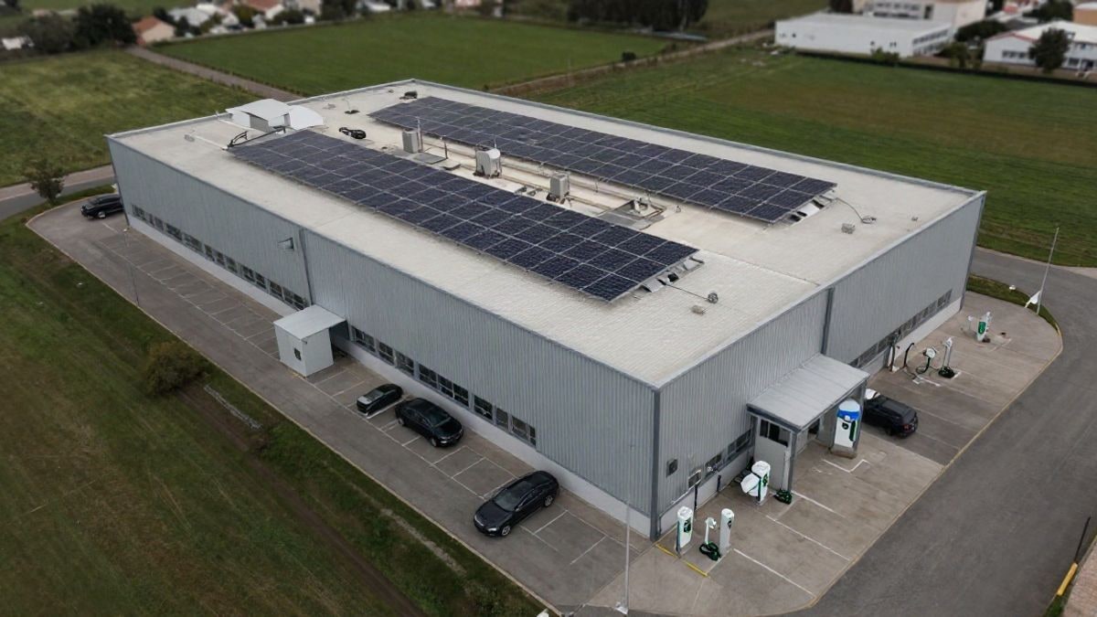 Imagen ilustrativa: vista cenital de un complejo industrial con placas solares en la cubierta y puntos de recarga para vehículos eléctricos